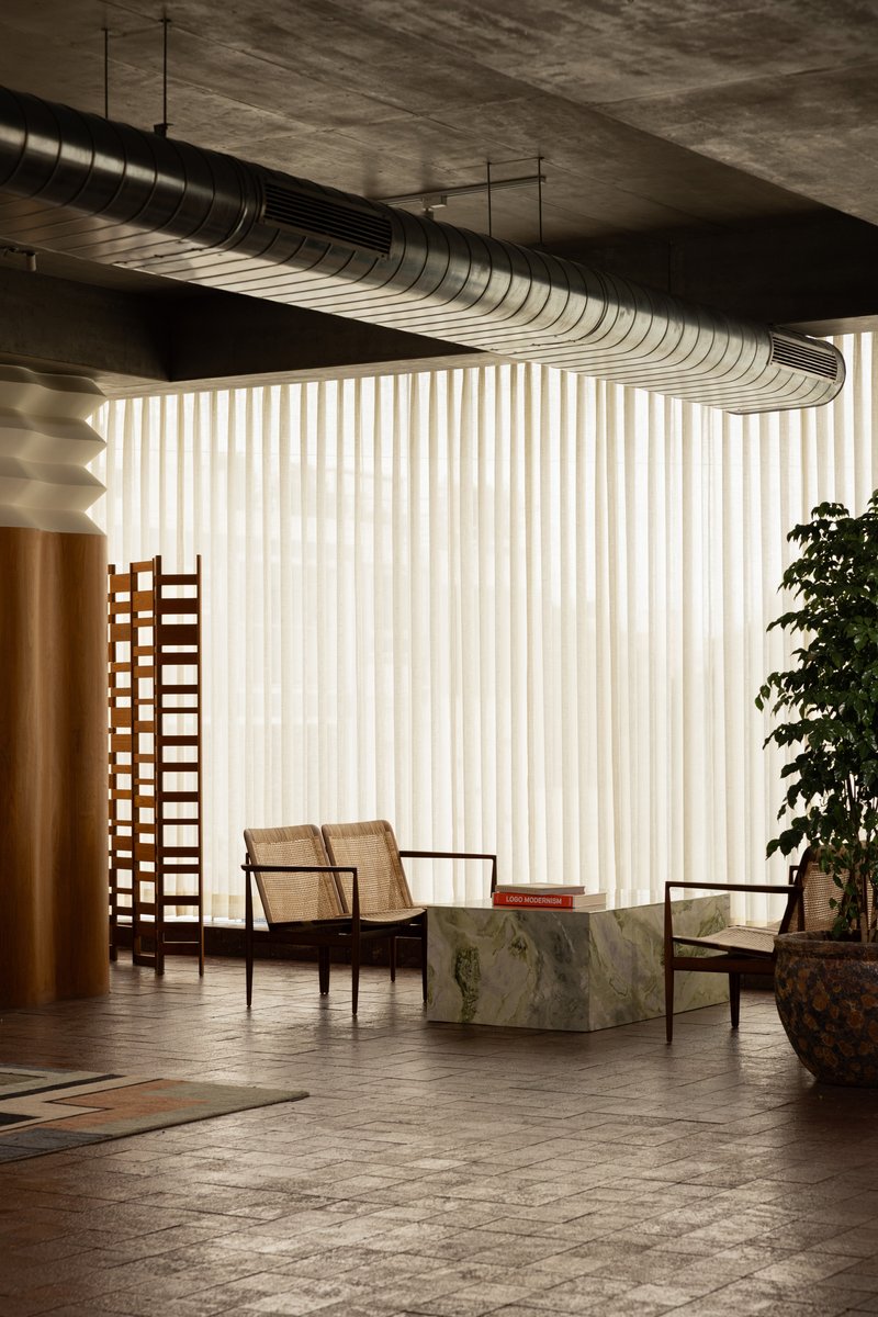 Interior seating area with exposed spiral ductwork overhead and vertical fabric curtain filtering natural light