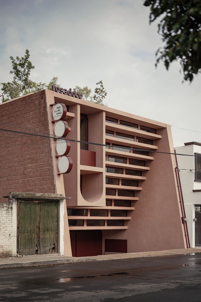 Street view of the pink stucco facade with horizontal louvers and circular motifs beside a brick wall