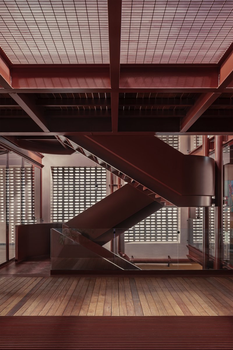 Central steel staircase with timber treads against a perforated block screen wall under exposed beams