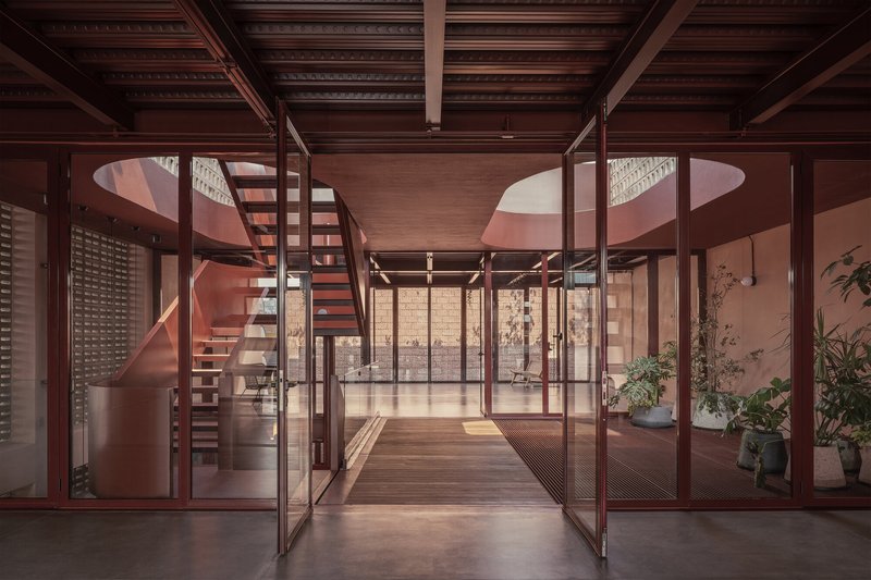 Glass-partitioned corridor with steel frame doors looking toward a spiral staircase