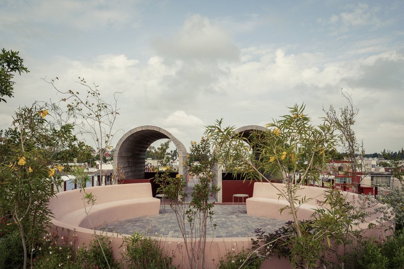 Rooftop terrace with pink curved seating walls and twin barrel vault arches framed by planted beds under cloudy skies