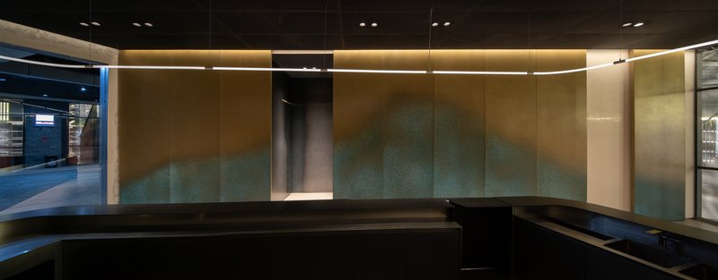 Curved reception counter against a backlit wall with oxidized copper and verdigris patina panels
