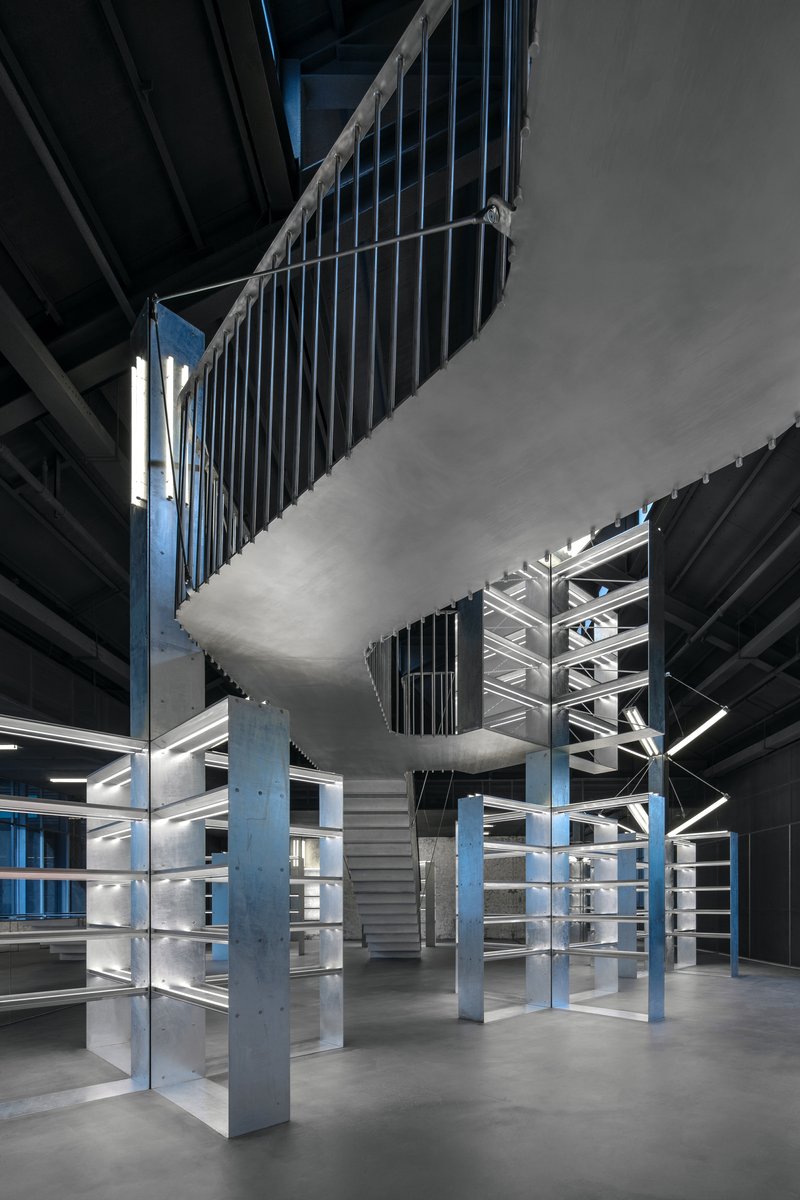 Interior view of the double-height space with vertical metal slat screens and blue steel columns