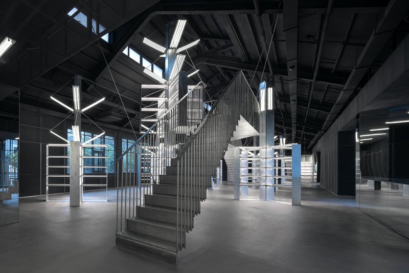 Sculptural staircase with vertical slat balustrade beneath exposed black ceiling structure and linear lighting
