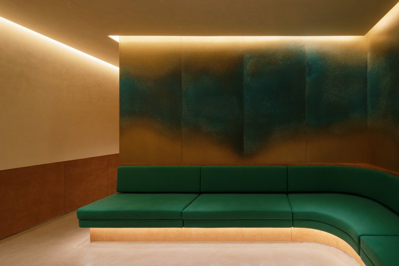Recessed cove lighting above a curved green velvet banquette against gradient painted wall panels