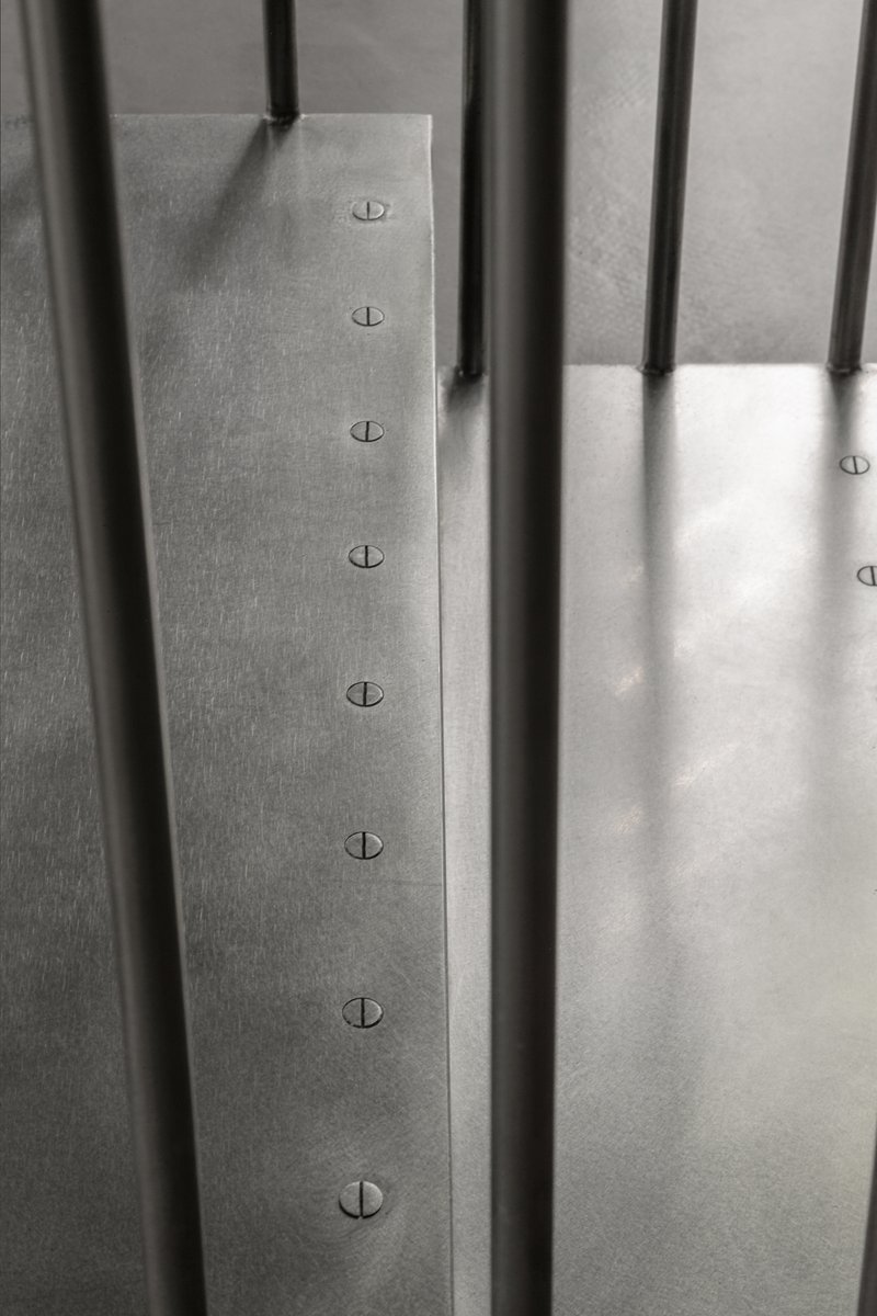 Detail of vertical steel rods penetrating a brushed metal plate with countersunk fasteners
