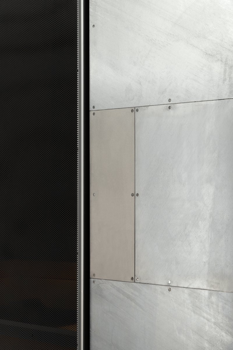 Junction between black perforated metal panel and raw concrete wall with exposed screws