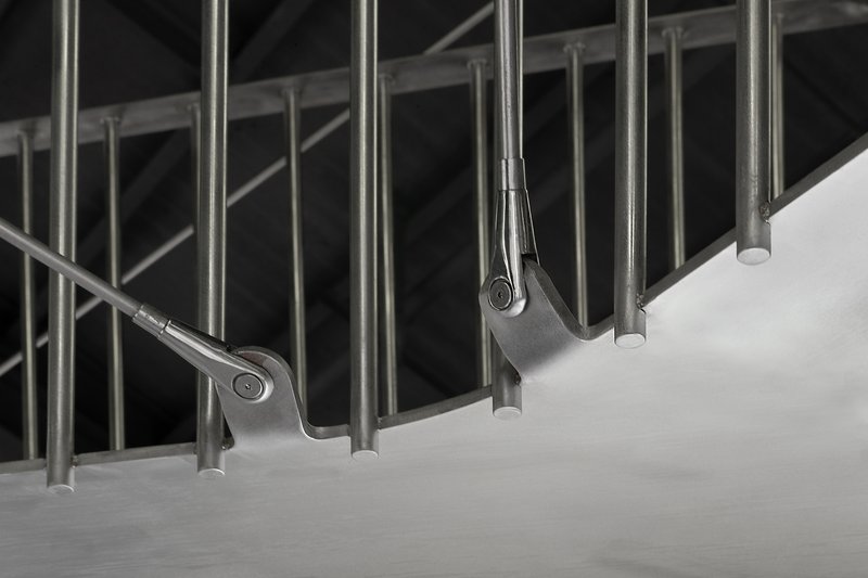 Upward view of cylindrical steel handrails cantilevering from curved concrete stair treads