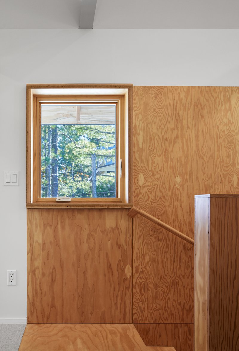Interior corner with oak plywood wall paneling and recessed staircase railing beneath a picture window