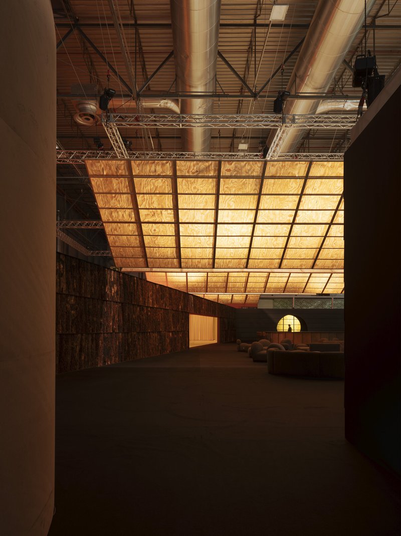 Illuminated wooden panel ceiling curving overhead in an industrial hall with exposed metal trusses and ducts