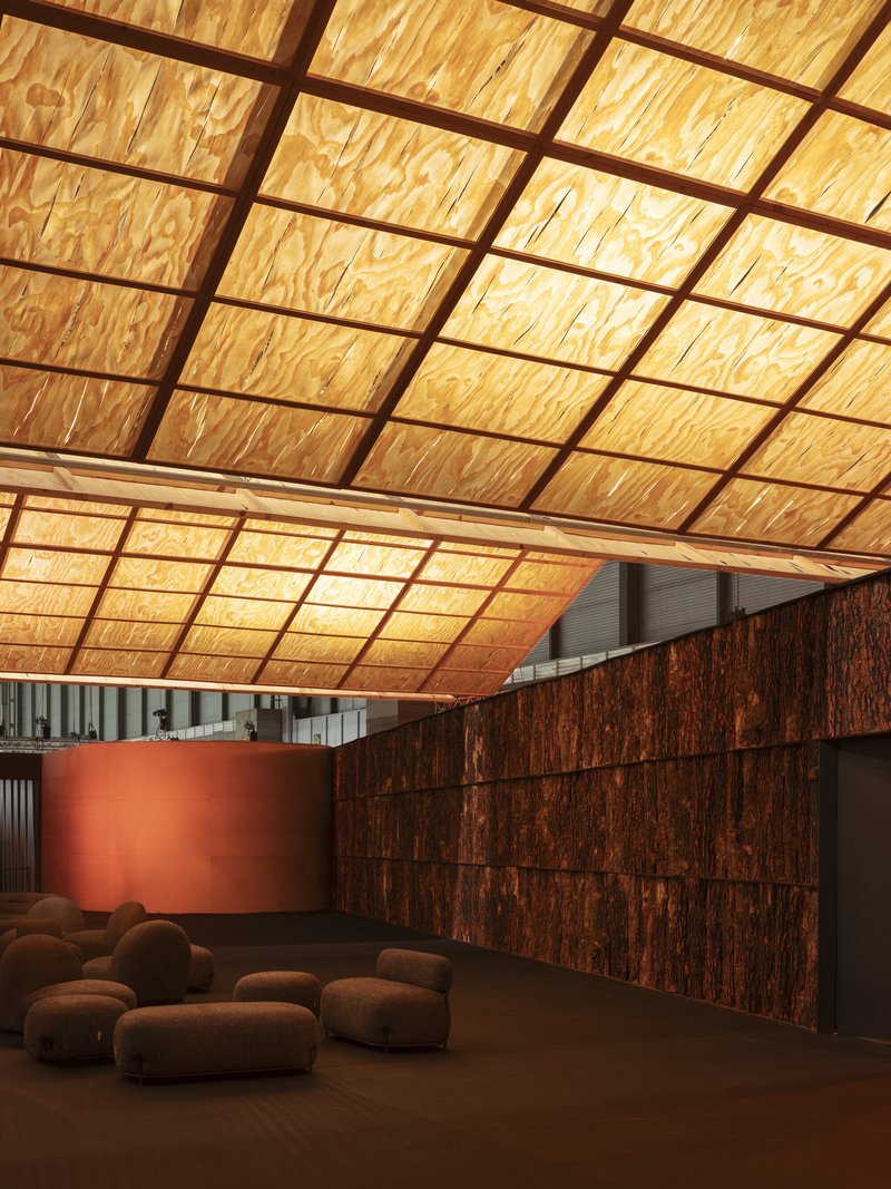 Close view of the translucent plywood panel grid ceiling sloping downward past a terracotta cylindrical wall