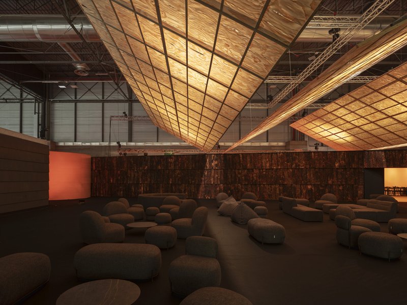 Intersecting backlit timber ceiling planes suspended above a lounge area with rounded ottomans and textured bark walls