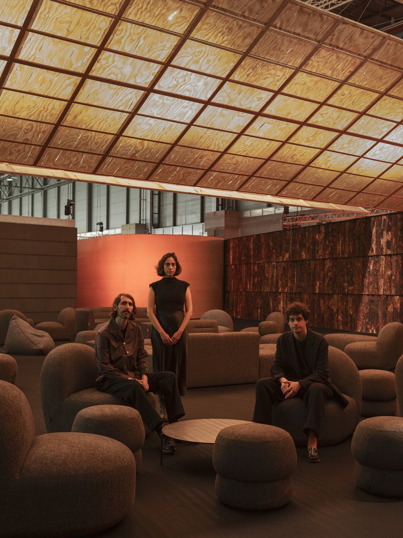 Lounge seating area with three visitors beneath a gridded timber ceiling and coral-painted wall
