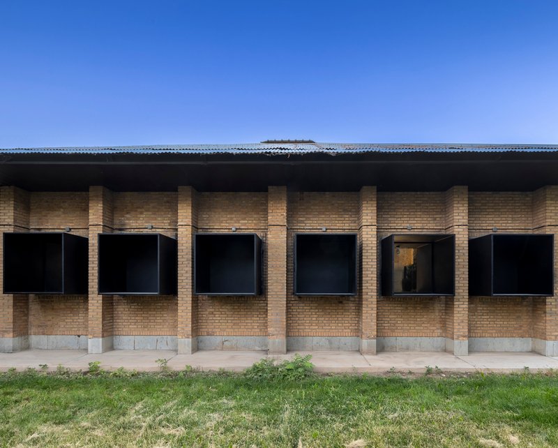 Facade with yellow brick columns and black metal-framed windows under a corrugated metal roof edge