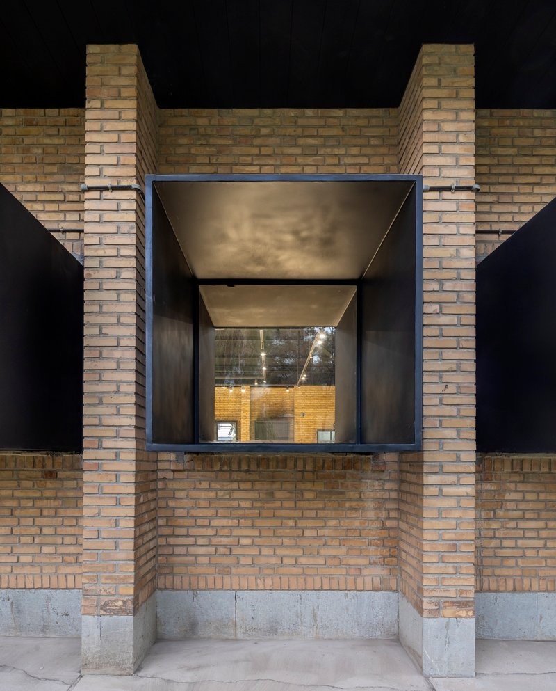 Recessed black steel window volume framed by yellow brick piers and concrete base at night