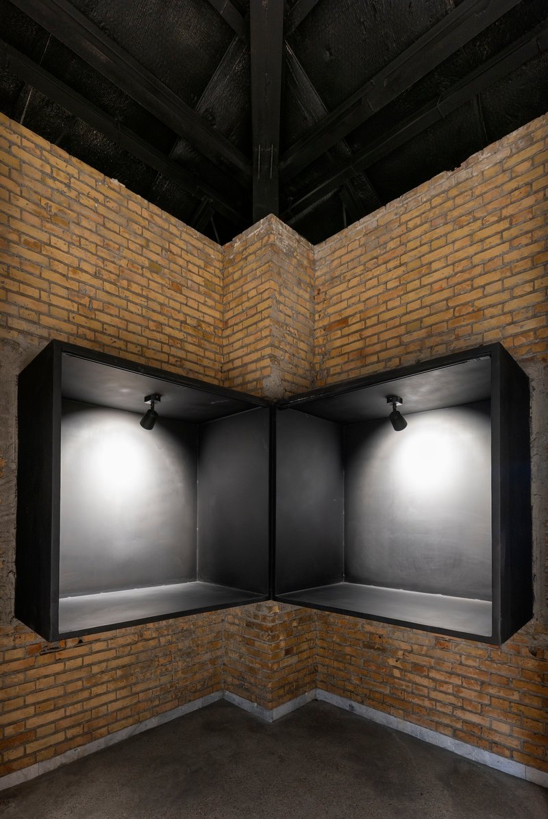 Corner display niche with black metal frame and spotlights set into yellow brick walls under exposed timber beams