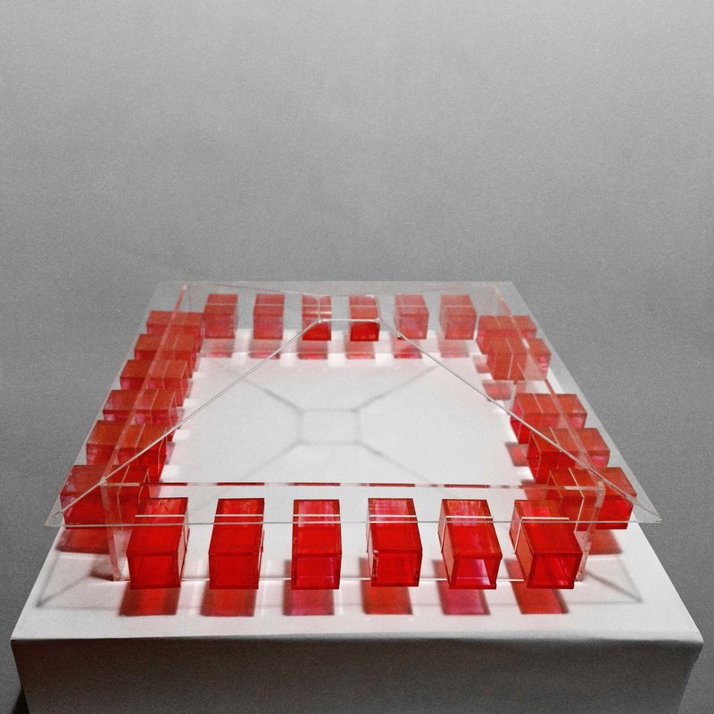The image showcases an architectural model featuring a grid-like arrangement of red cubes suspended within a clear acrylic structure. The design emphasizes geom