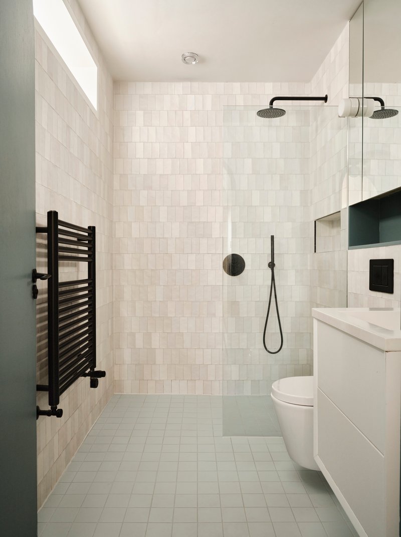 Bathroom with white square tile walls, black fixtures, towel radiator and skylight above shower area