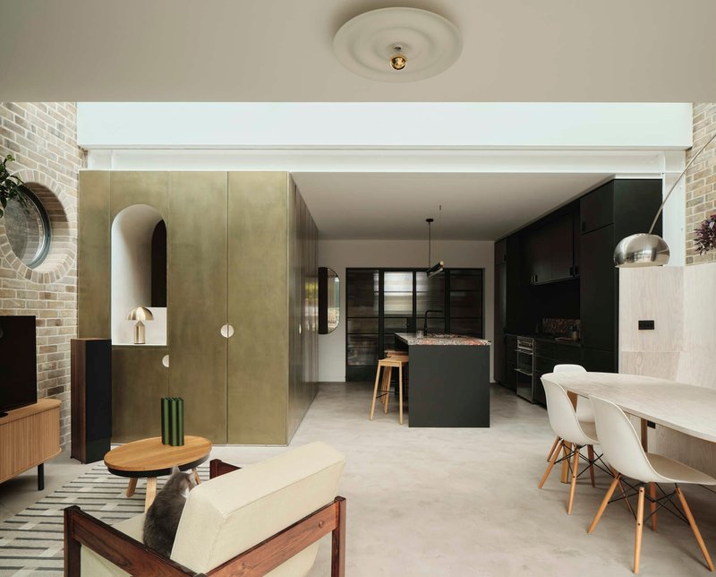 Open-plan living area with brass-clad volumes and continuous pale flooring under indirect perimeter lighting