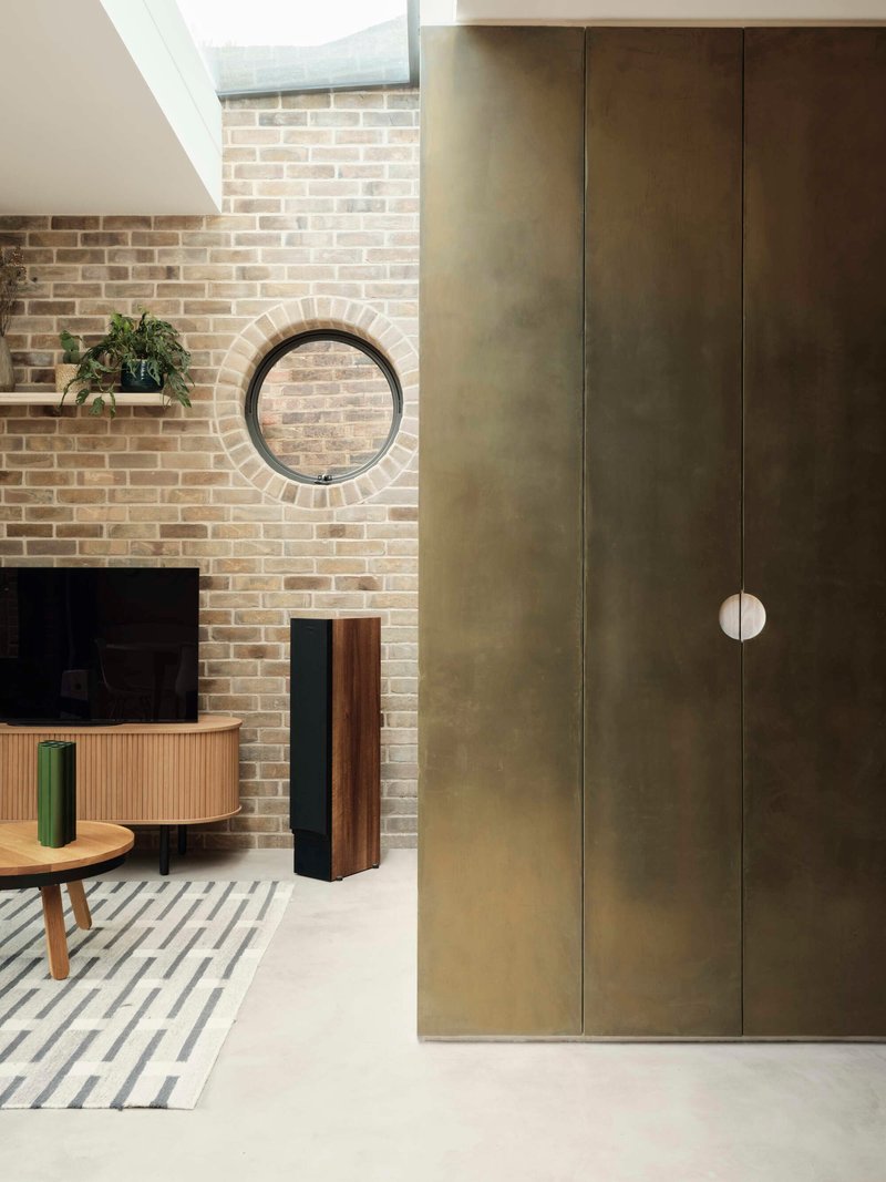 Living space showing tall brass-clad joinery beside a buff brick fireplace wall with circular window