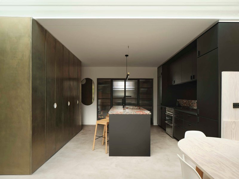 Kitchen with dark timber cabinetry, terrazzo island bench and pale polished concrete flooring