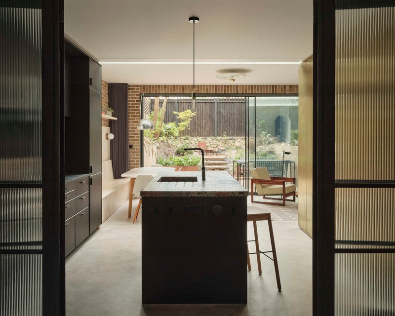 View through fluted glass doors toward kitchen island and planted rear courtyard beyond