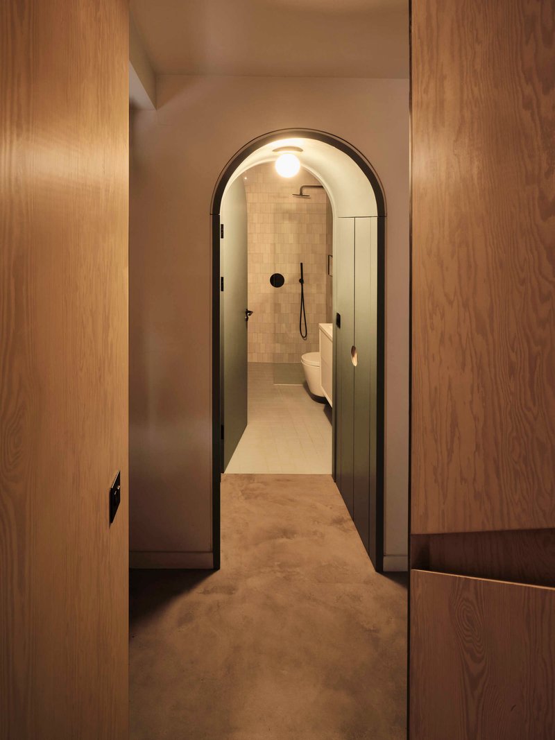 Arched doorway with black frame opening into bathroom with cream tiled walls