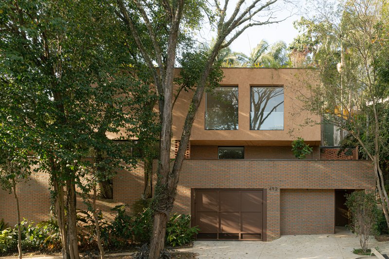 Street facade with brick base and timber-clad upper volume framed by mature trees