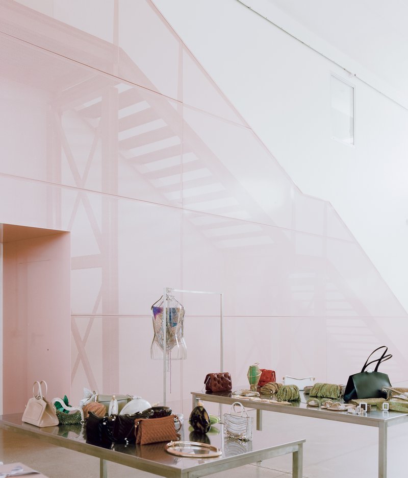 Translucent pink partition wall enclosing display tables with handbags and garments beneath a sloping ceiling