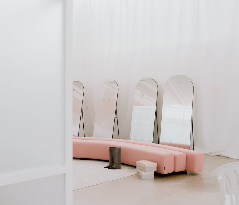 Pink upholstered seating base with arched mirrors leaning against the white wall