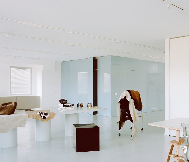 Pale blue glass partition enclosing workspace with cowhide draped over maroon cube