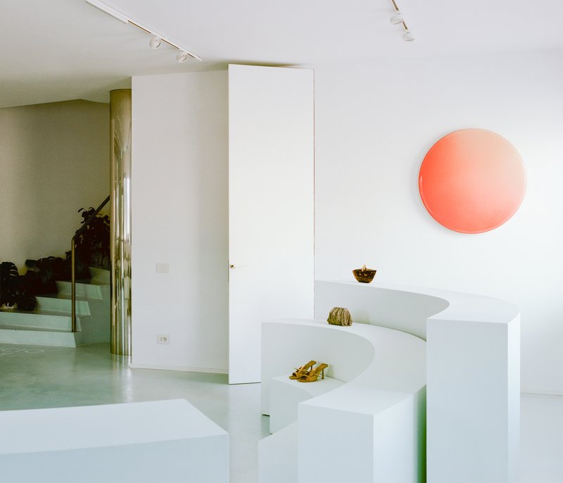 White stepped display platform with coral circular wall light above concrete floor