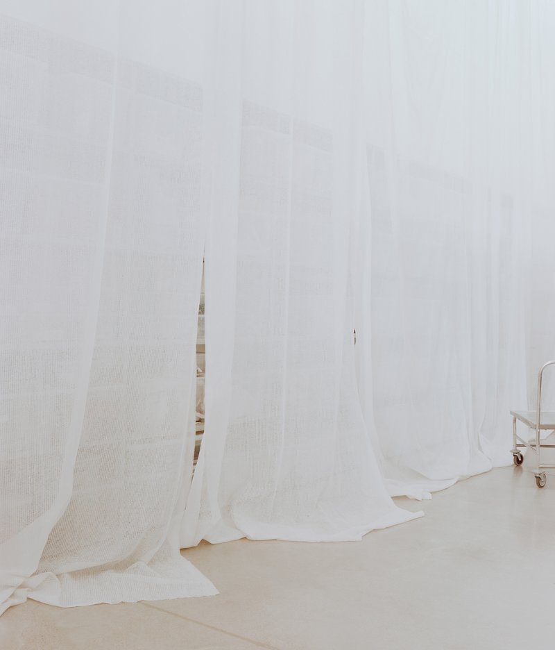 Floor-to-ceiling white mesh curtains hanging in soft folds across the workroom