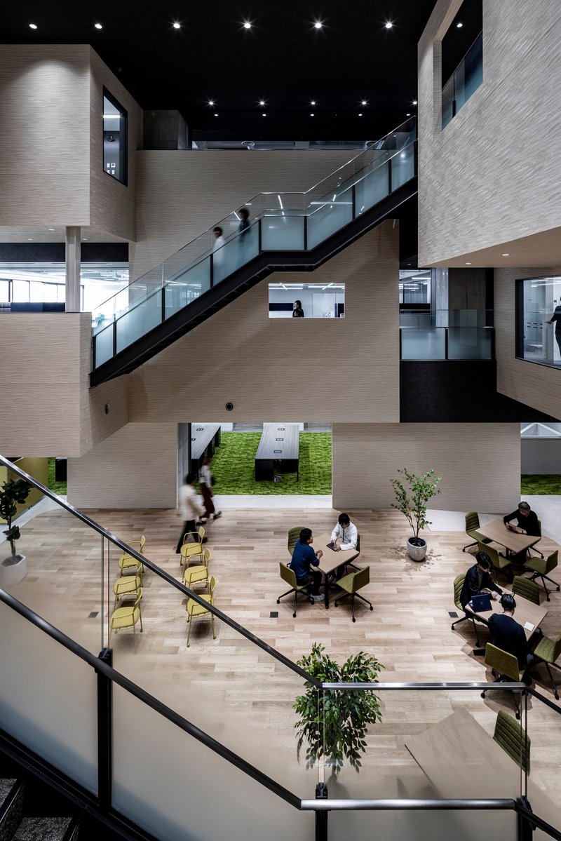 Atrium interior with metal-and-glass staircases linking floors, people seated at tables and a grass-covered courtyard below