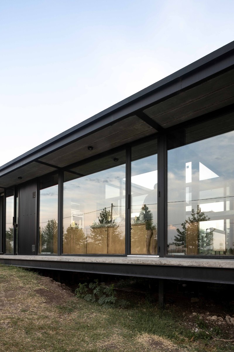 Corner detail of the glazed facade with black metal frames and concrete soffit at twilight