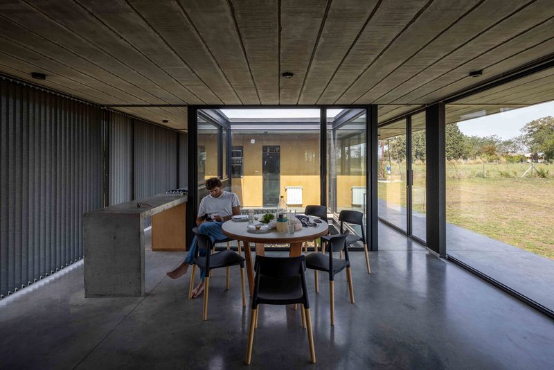Dining area with concrete floor and timber ceiling opening to landscape through floor-to-ceiling glass