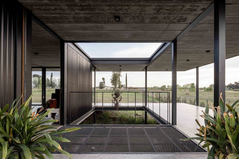 Covered entry passage framing a planted courtyard with metal grating and distant fields beyond