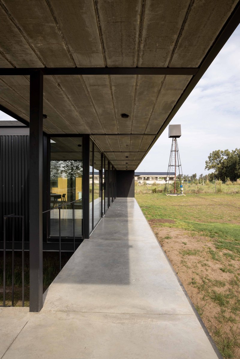 Covered concrete walkway with steel columns and water tower visible across the open landscape