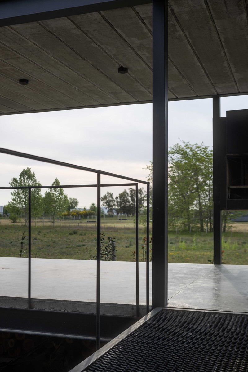 View through steel-framed glass door opening onto covered terrace under overcast sky