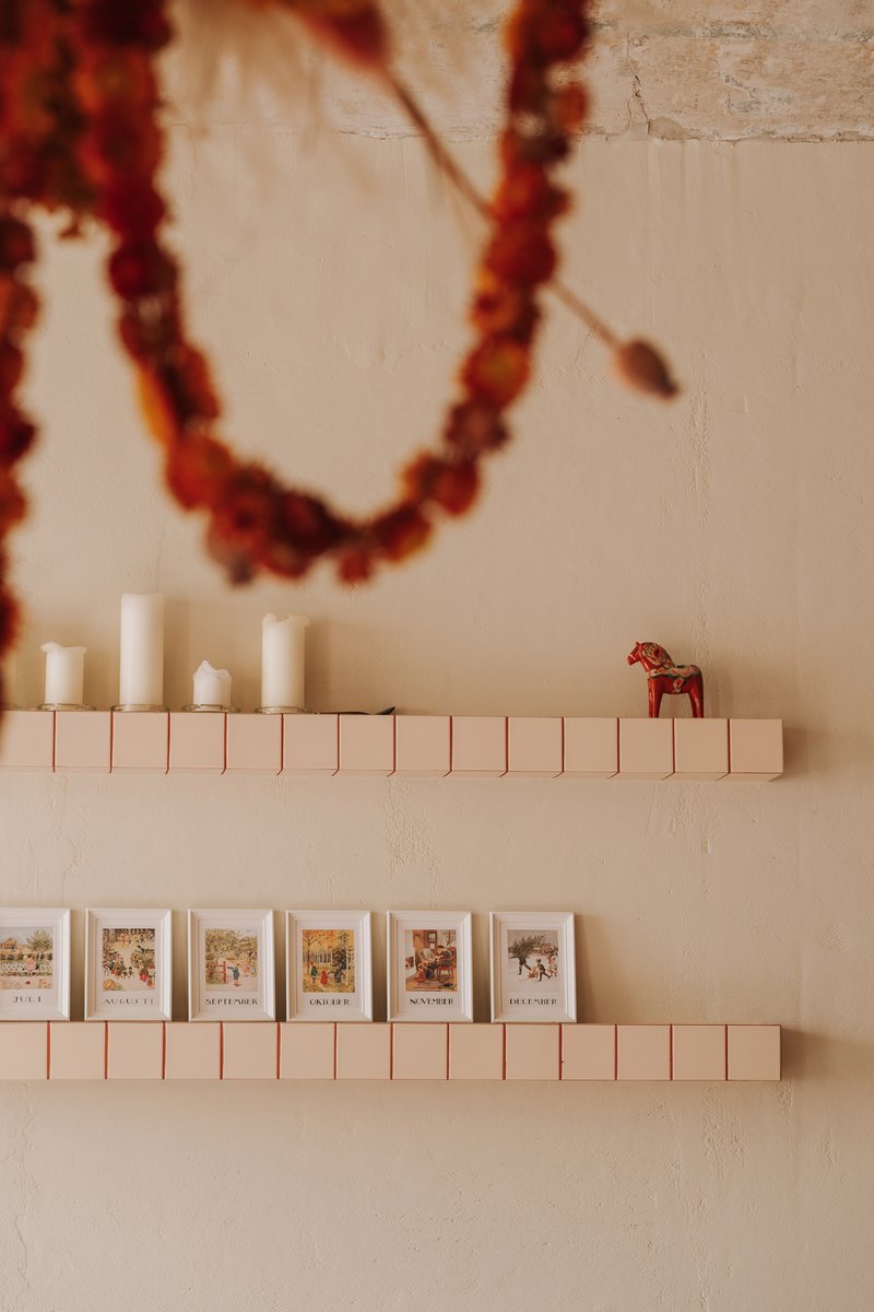 Wall-mounted shelves constructed from rectangular tiles displaying candles and printed cards
