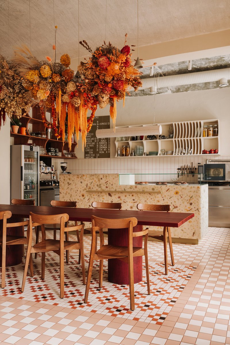 Open kitchen with terrazzo-clad counter and timber shelving below suspended dried flower arrangement with ribbon streamers