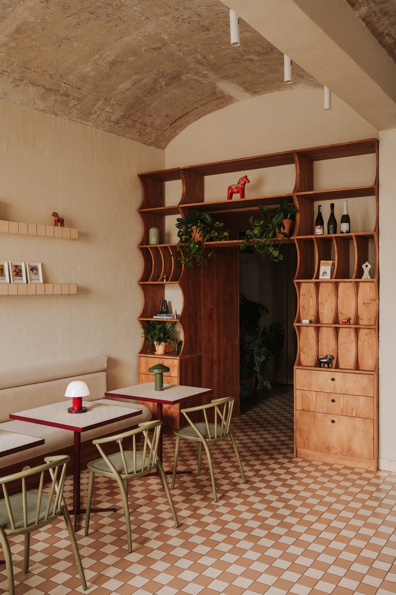 Curved timber shelving unit with integrated doorway under an exposed brick barrel vault ceiling