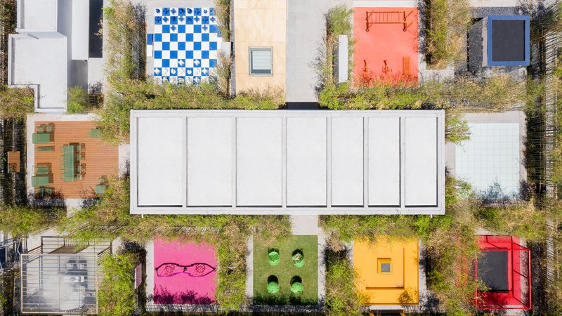 Drone view of the white skylight bar flanked by planted terraces and colored tile courts in autumn grasses