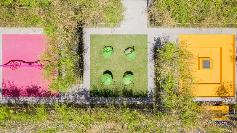 Top-down view of three tiled pavilions in pink, green, and yellow surrounded by overgrown vegetation