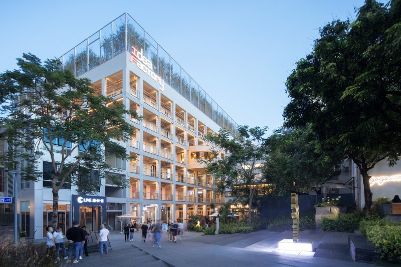 White facade with glass balconies and timber-lined balconies at dusk with pedestrians on the plaza below