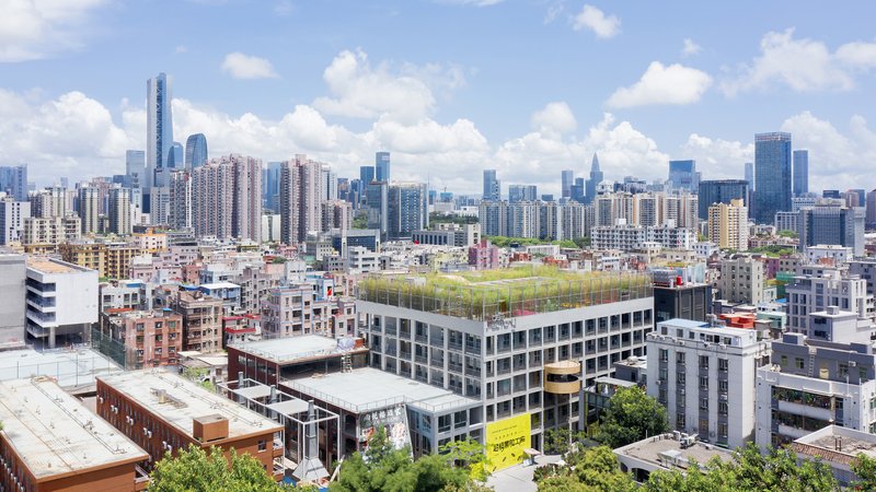Rooftop green field on a rectangular building surrounded by dense urban fabric under scattered clouds