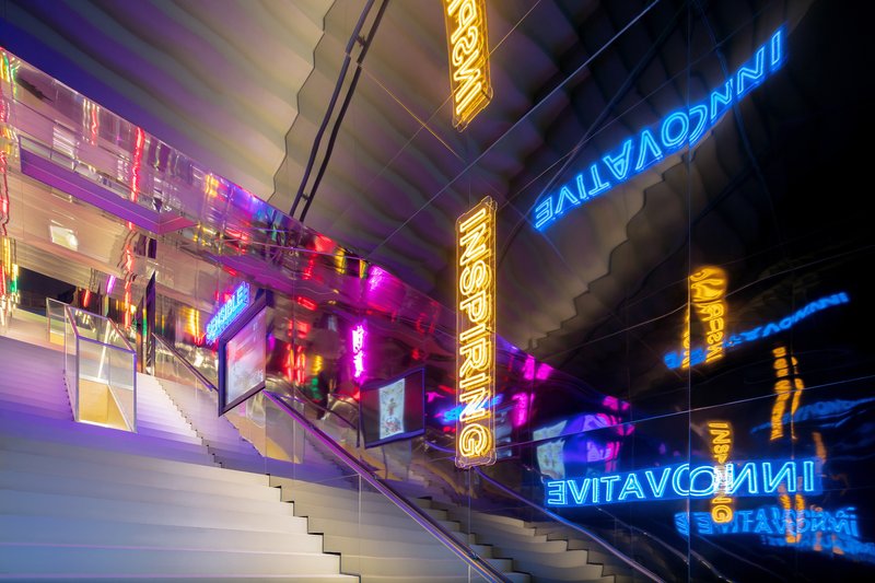 Exterior staircase with glass railings and reflected neon signage in multiple colors at night