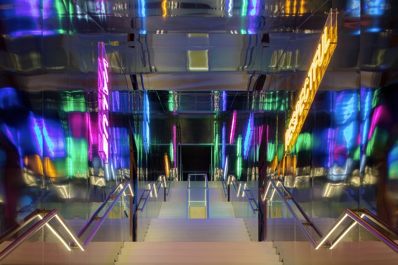 View up the central staircase with mirrored ceiling reflecting multicolored neon light installations