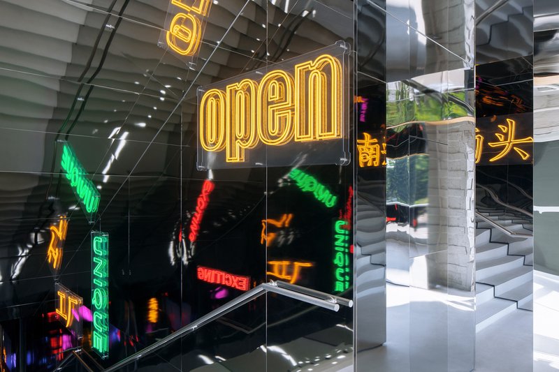 Neon signage suspended in clear acrylic frames beside concrete columns and a stepped interior