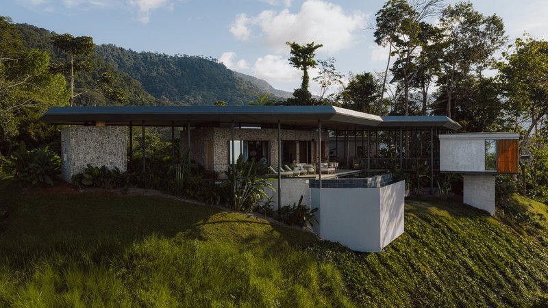 Elevated residence with stone walls and flat roof set on a hillside surrounded by trees